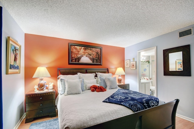 bedroom with ensuite bath, light hardwood / wood-style flooring, and a textured ceiling