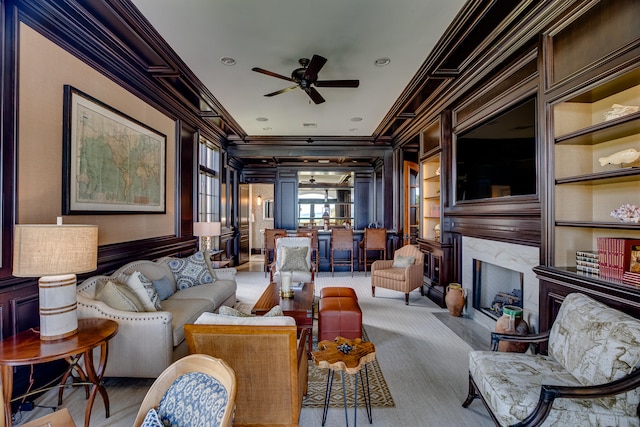 carpeted living room with ornamental molding, ceiling fan, a premium fireplace, and built in features