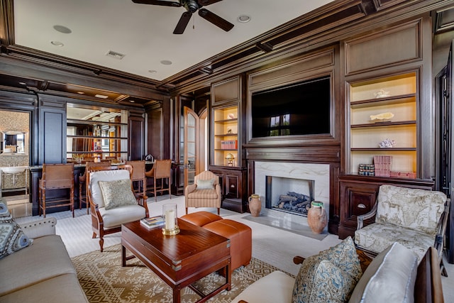 living room with built in shelves, ornamental molding, ceiling fan, and a fireplace