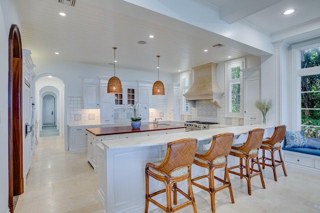 kitchen featuring hanging light fixtures, white cabinets, custom range hood, a kitchen island, and tasteful backsplash