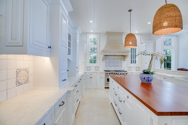 kitchen with custom exhaust hood, double oven range, butcher block counters, tasteful backsplash, and pendant lighting