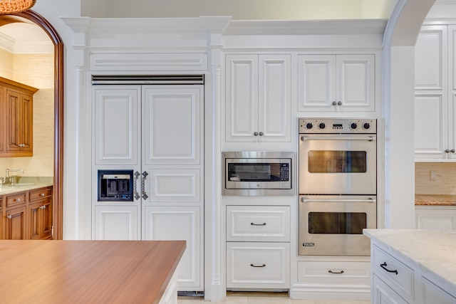 kitchen featuring double wall oven, tasteful backsplash, white cabinets, stainless steel microwave, and sink