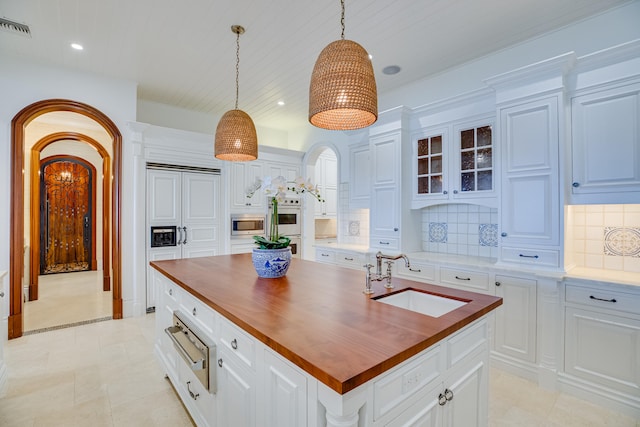 kitchen with stainless steel microwave, backsplash, sink, an island with sink, and pendant lighting