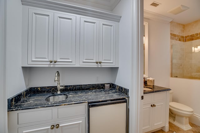 kitchen featuring white cabinets, dark stone counters, dishwashing machine, and ornamental molding