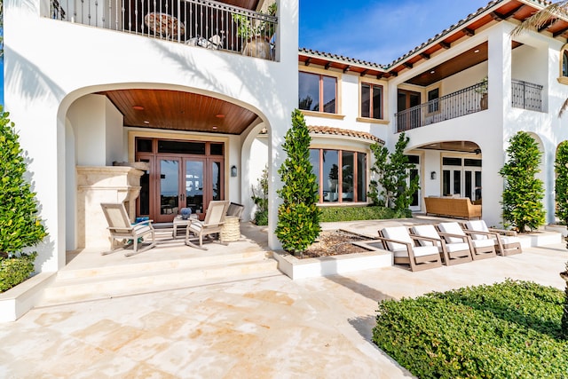 rear view of house with a balcony, a patio area, and french doors