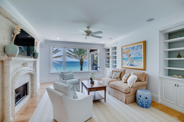 living room with ceiling fan, light wood-type flooring, a water view, a premium fireplace, and built in shelves