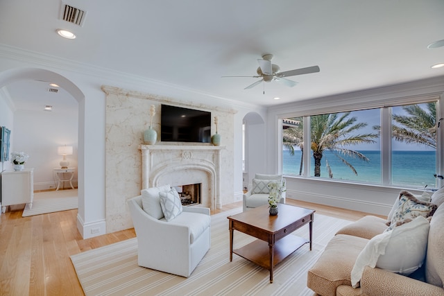 living room featuring ceiling fan, a fireplace, a water view, light hardwood / wood-style flooring, and crown molding