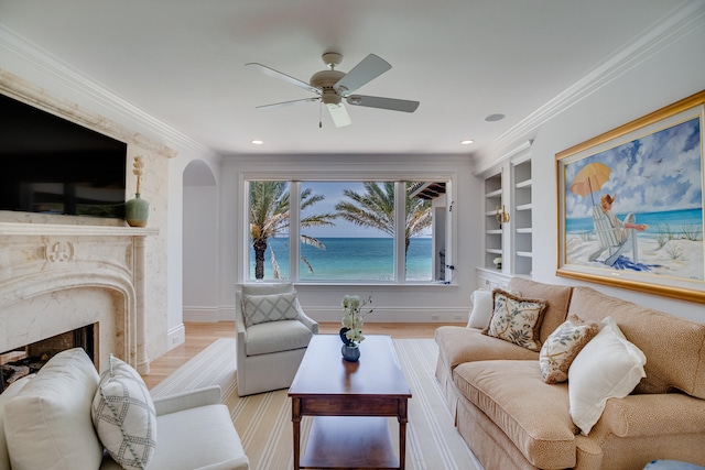 living room featuring ceiling fan, a premium fireplace, built in features, light hardwood / wood-style floors, and a water view