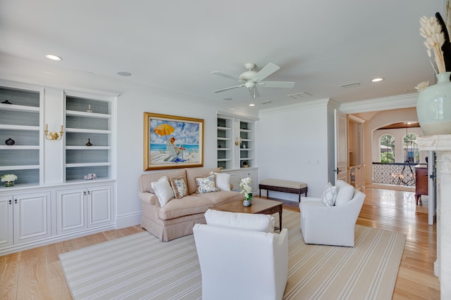 living room with built in features, ceiling fan, light wood-type flooring, and crown molding