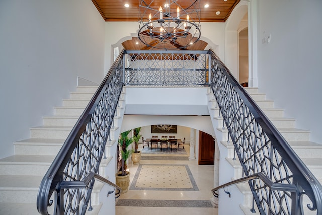 stairway featuring an inviting chandelier, wood ceiling, a towering ceiling, and ornamental molding