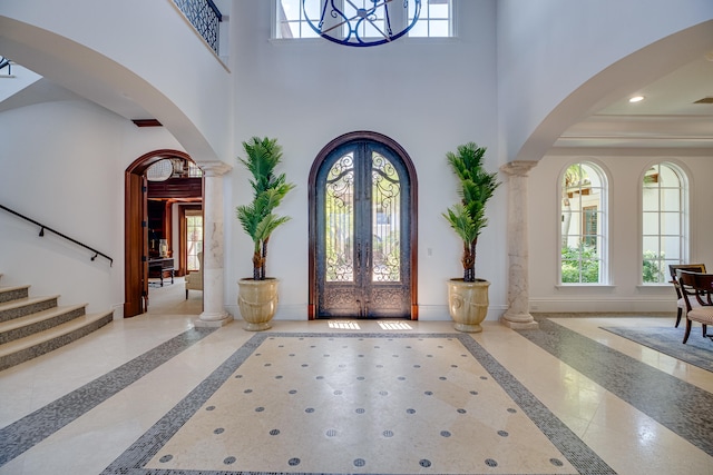 entryway featuring light tile floors, a notable chandelier, french doors, and decorative columns