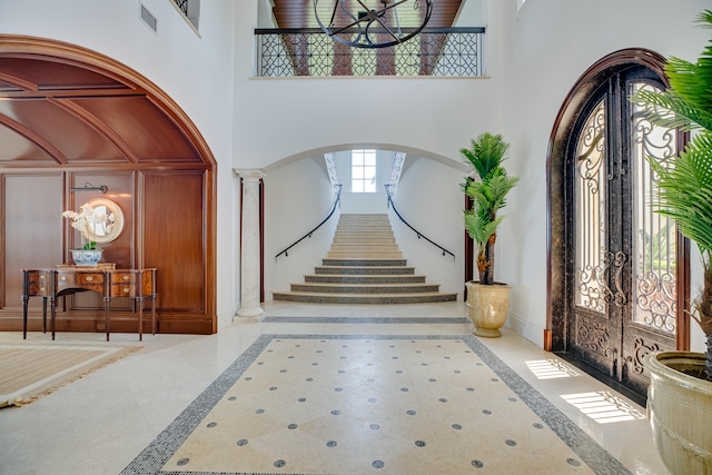 tiled entrance foyer with a notable chandelier, decorative columns, a high ceiling, and french doors