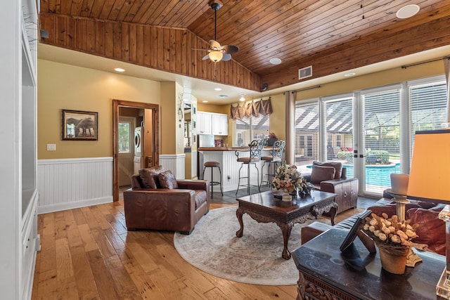 living room with light wood-type flooring, stacked washing maching and dryer, wood ceiling, vaulted ceiling, and ceiling fan