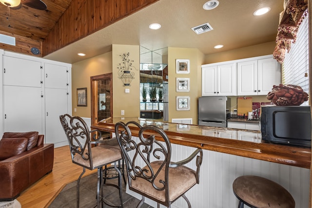 kitchen with white cabinets, light hardwood / wood-style flooring, ceiling fan, stainless steel fridge, and a textured ceiling