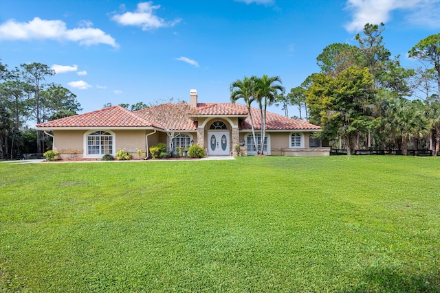 mediterranean / spanish-style house featuring stucco siding, a chimney, a front lawn, and a tiled roof