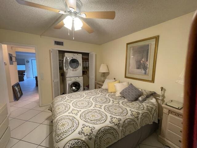 tiled bedroom with ceiling fan, a textured ceiling, stacked washer / drying machine, and a closet