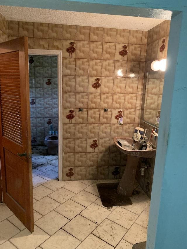 bathroom featuring tile patterned flooring, toilet, and tile walls