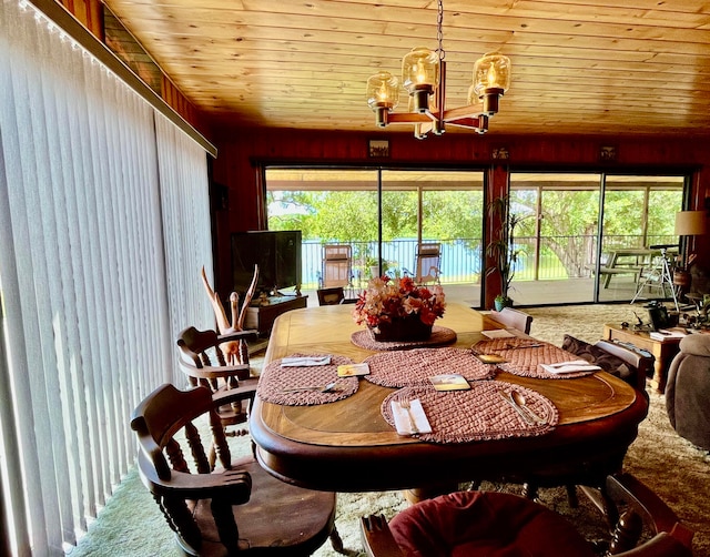 carpeted dining room with wood walls, a notable chandelier, a healthy amount of sunlight, and wooden ceiling