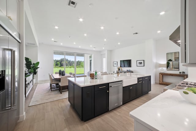 kitchen featuring light stone counters, sink, light hardwood / wood-style floors, stainless steel appliances, and a kitchen island with sink