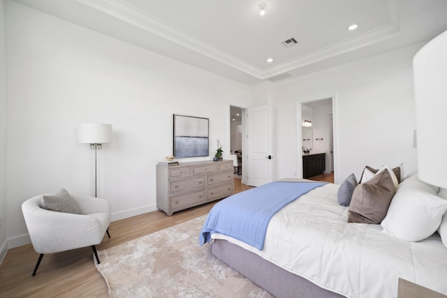 bedroom with light hardwood / wood-style floors, ensuite bathroom, and a tray ceiling