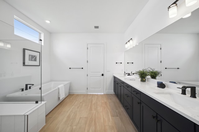 bathroom with hardwood / wood-style floors, a bath to relax in, and dual vanity