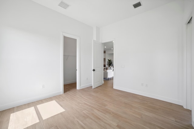 unfurnished bedroom with a spacious closet, a closet, and light wood-type flooring