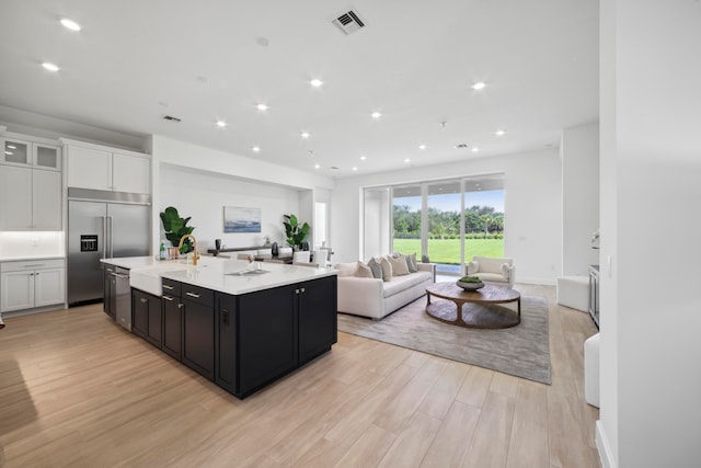 kitchen featuring stainless steel built in fridge, light hardwood / wood-style floors, a kitchen island with sink, white cabinets, and sink