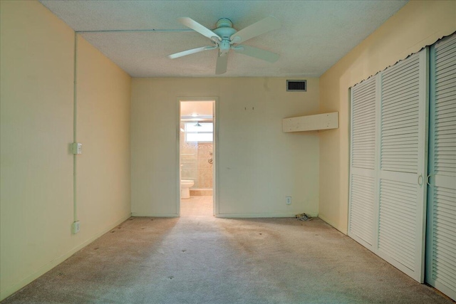 unfurnished bedroom featuring light colored carpet, ceiling fan, a closet, and ensuite bathroom