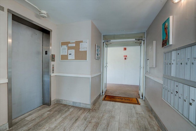 corridor featuring mail boxes, elevator, and light wood-type flooring