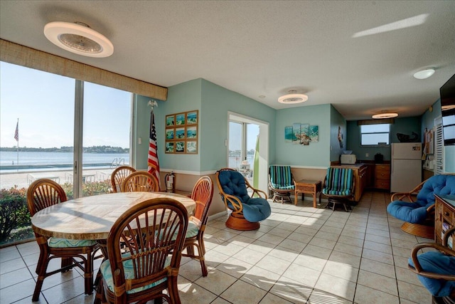 dining space featuring plenty of natural light, a textured ceiling, a water view, and light tile patterned floors