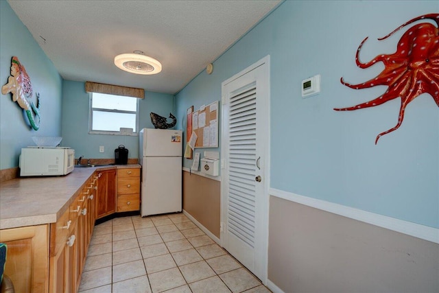 kitchen featuring white appliances, sink, light tile patterned flooring, and a textured ceiling