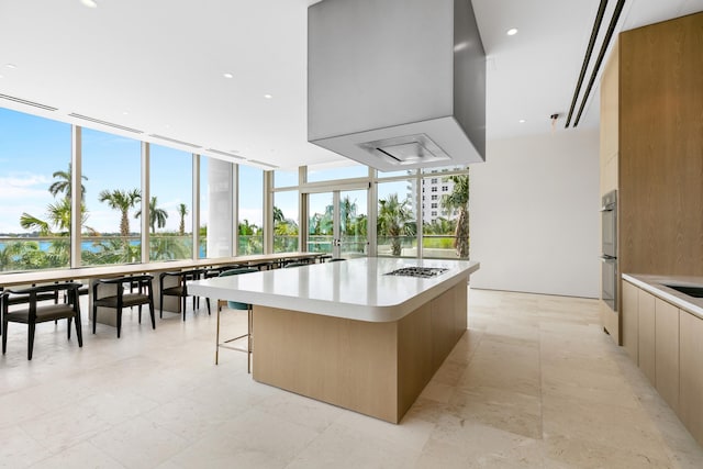 kitchen with a kitchen breakfast bar, a kitchen island with sink, a wall of windows, and light tile floors