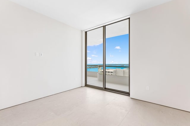 spare room featuring light tile flooring, a water view, and floor to ceiling windows