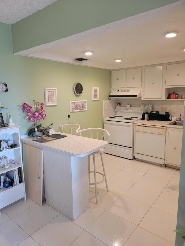 kitchen featuring range hood, light tile patterned floors, light countertops, white appliances, and a peninsula