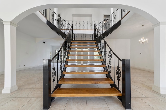 stairway with light tile flooring, a high ceiling, ornate columns, and an inviting chandelier