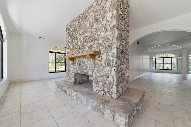 unfurnished living room with light tile floors, lofted ceiling, and a stone fireplace