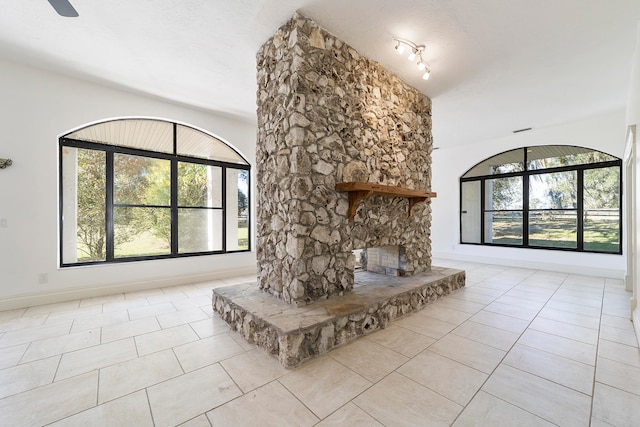 unfurnished living room with ceiling fan, track lighting, light tile floors, and a stone fireplace