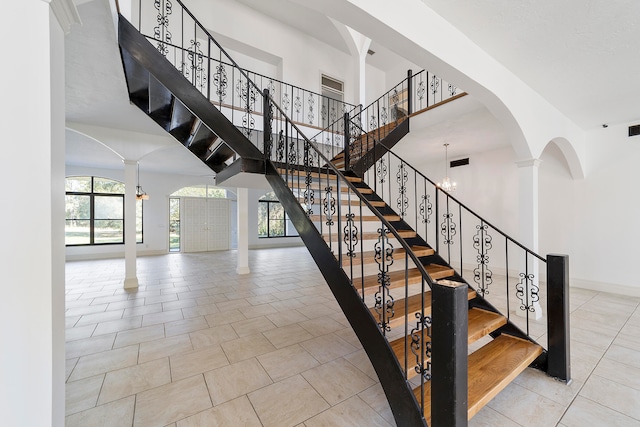 staircase featuring an inviting chandelier, ornate columns, light tile floors, and a high ceiling