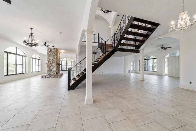 stairs featuring decorative columns, a healthy amount of sunlight, ceiling fan with notable chandelier, and light tile flooring