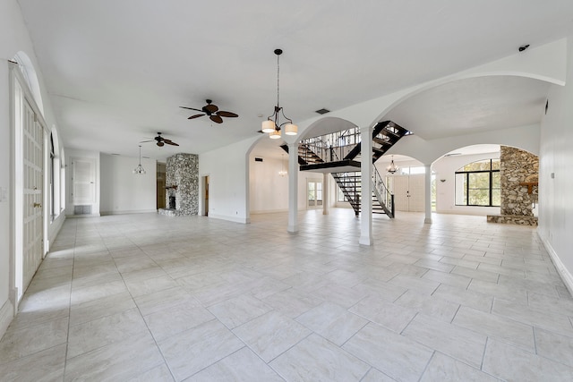 unfurnished room with light tile floors, a stone fireplace, and ceiling fan with notable chandelier