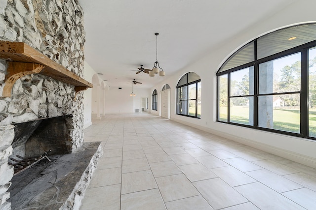 unfurnished living room featuring ceiling fan, light tile floors, and a stone fireplace