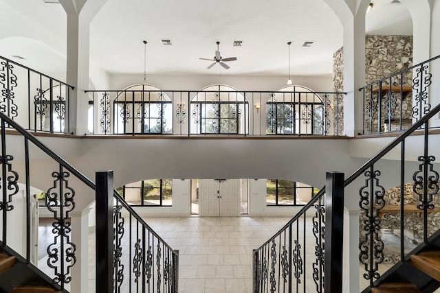 stairs with tile floors, ceiling fan with notable chandelier, a towering ceiling, and a wealth of natural light