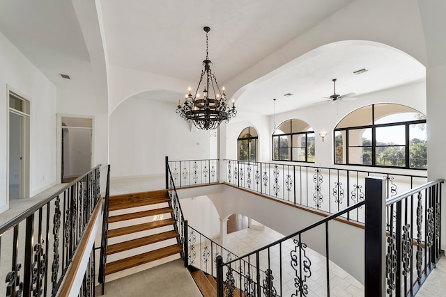 staircase with light carpet and ceiling fan with notable chandelier