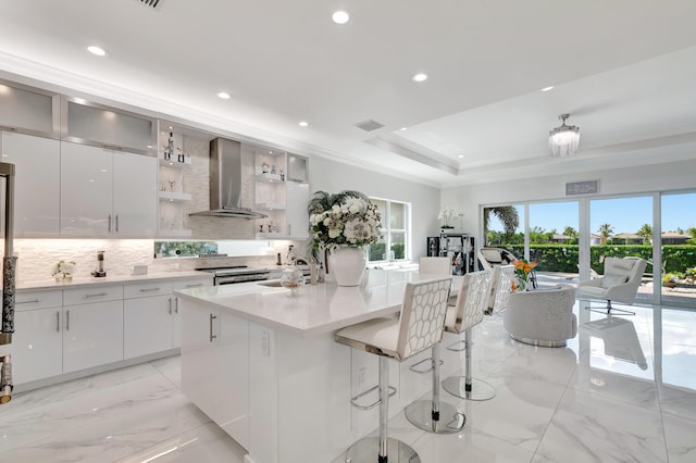 kitchen featuring wall chimney range hood, a kitchen breakfast bar, white cabinetry, and a tray ceiling