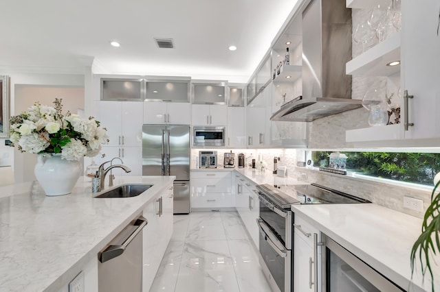 kitchen featuring stainless steel appliances, wall chimney range hood, tasteful backsplash, white cabinets, and sink