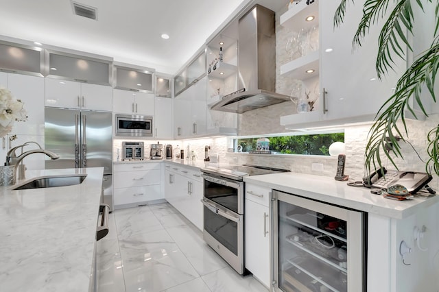 kitchen featuring beverage cooler, wall chimney exhaust hood, appliances with stainless steel finishes, white cabinetry, and backsplash