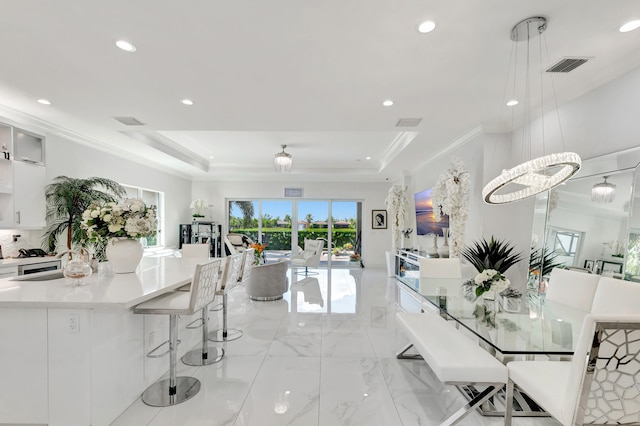 interior space featuring a kitchen breakfast bar, decorative light fixtures, a notable chandelier, white cabinets, and a tray ceiling