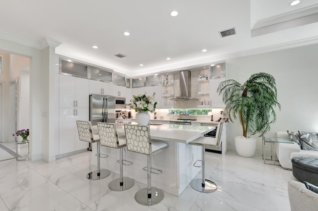 kitchen with light tile floors, appliances with stainless steel finishes, a breakfast bar area, wall chimney range hood, and a center island