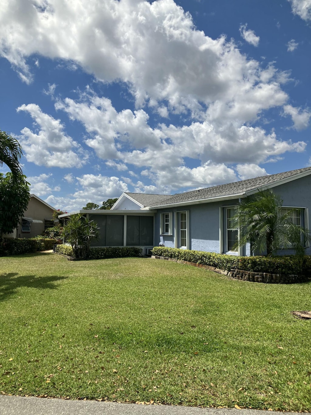 ranch-style house featuring a front lawn, a sunroom, and stucco siding