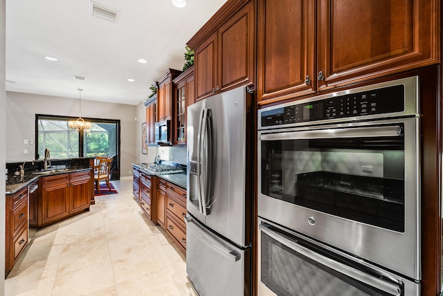 kitchen with dark stone counters, appliances with stainless steel finishes, light tile flooring, an inviting chandelier, and decorative light fixtures